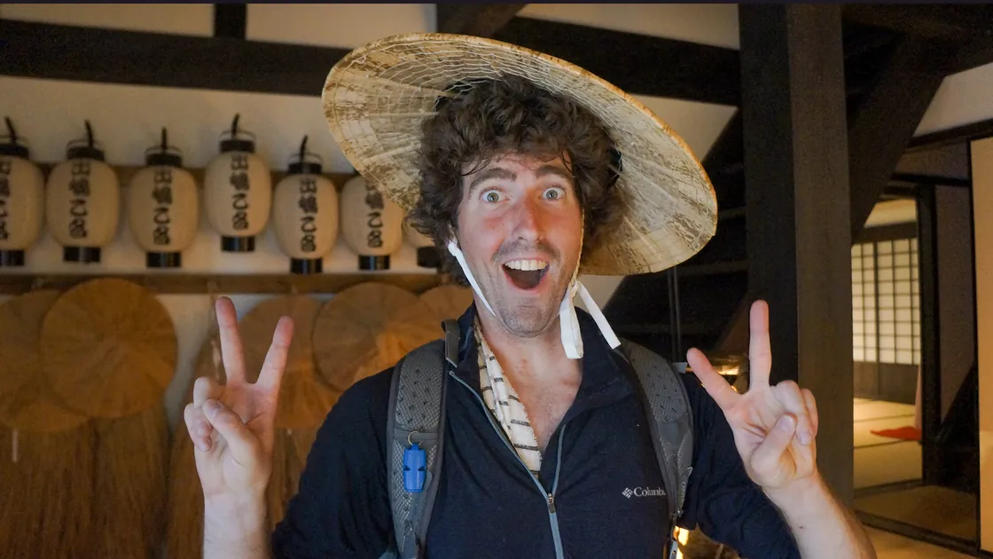 The same moment without the scale: Jef in a straw hat throwing
                  two peace signs at the camera in a lantern-lined room in Kumamoto.
